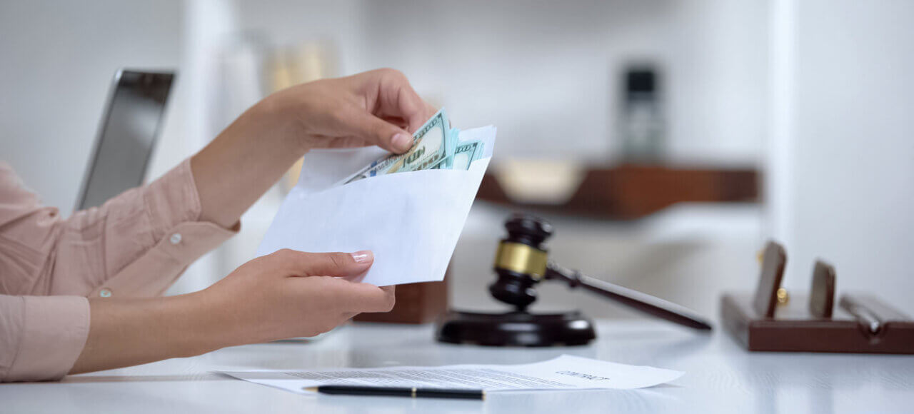 Hands placing cash into envelope near gavel, symbolizing spousal support or alimony payments